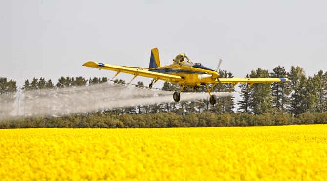 An image of a crop-dusting airplane spraying chemicals over a field.