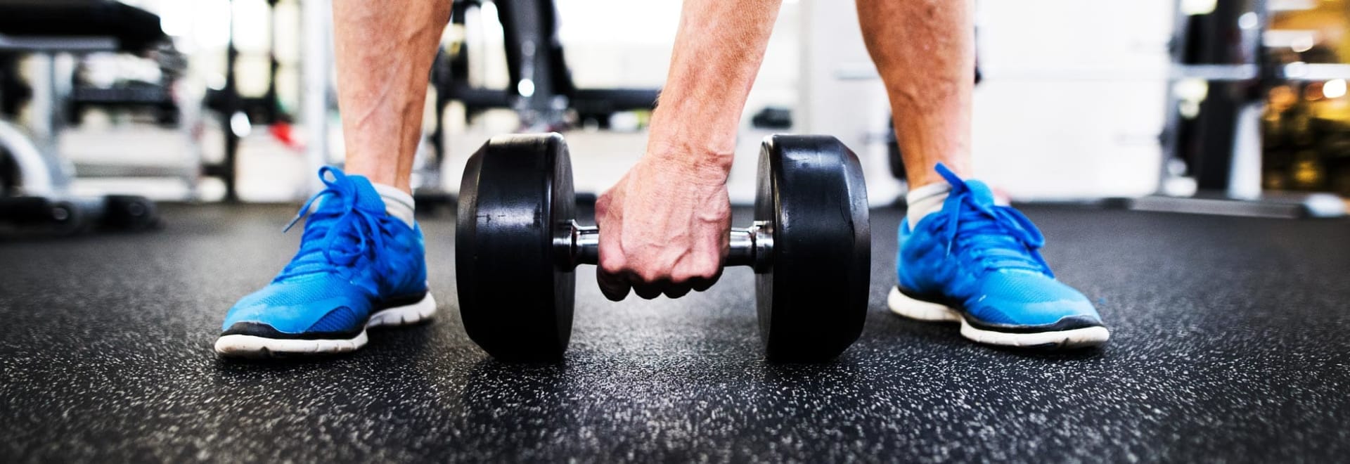 A man in blue sneakers about to lift a weight.