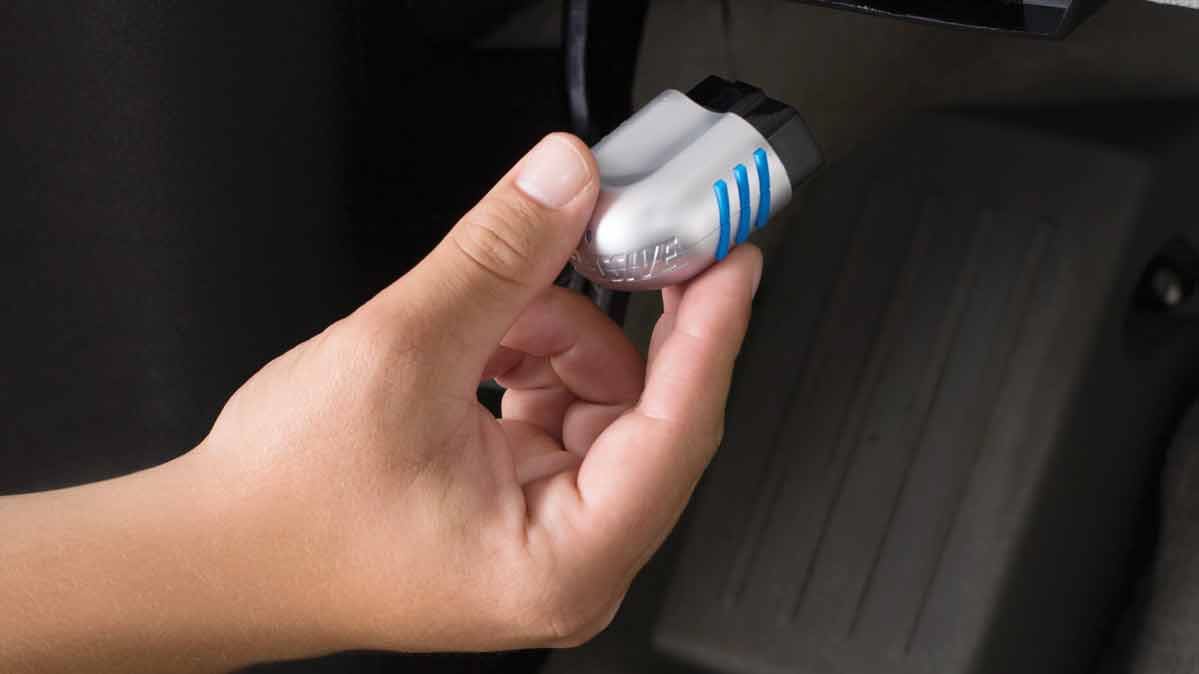 Hand inside a car, holding Progressive Snapshot device that tracks driving behavior.