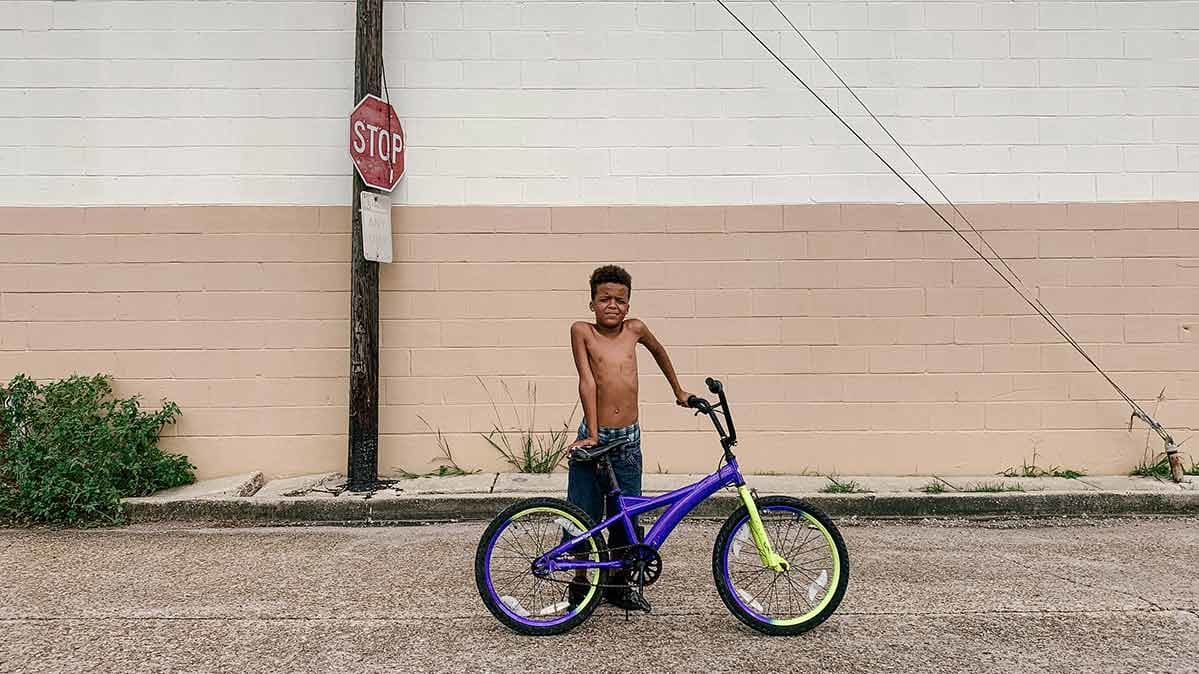 Boy leaning on bike on street.