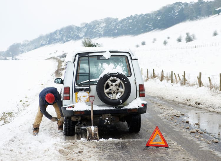 An image of a driver alongside his stalled vehicle on a snowy roadside