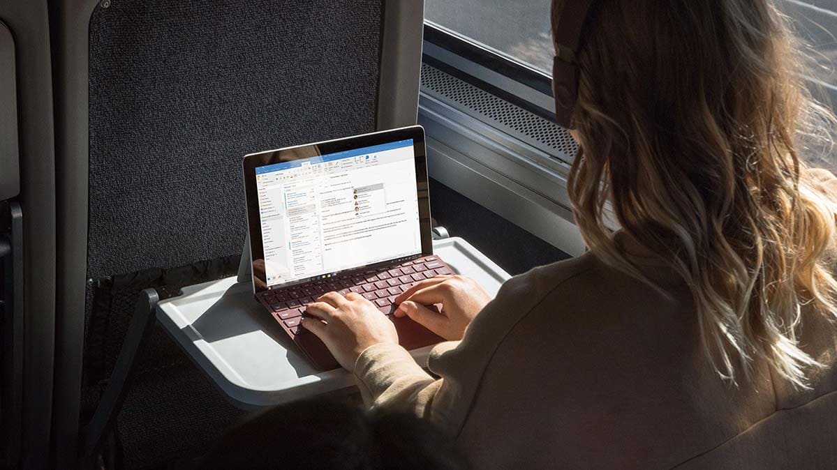 A woman sitting at the keyboard of a Microsoft Surface Go.