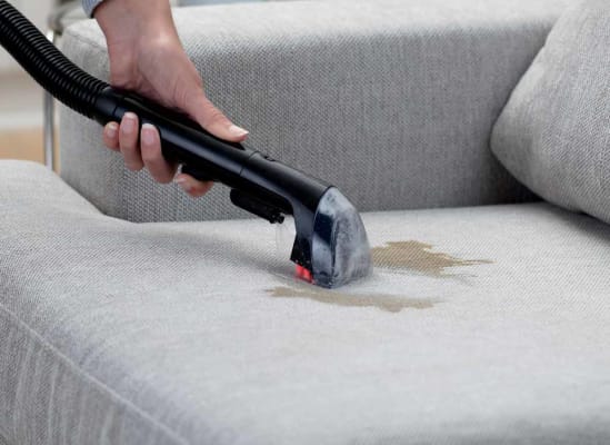 A person using a carpet cleaner attachment on a couch.