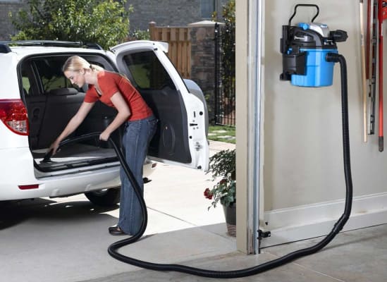A woman cleaning her car using a wet/dry vacuum that's mounted on the garage wall.