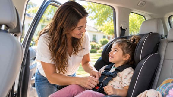 A woman helping a child buckle into a car seat.