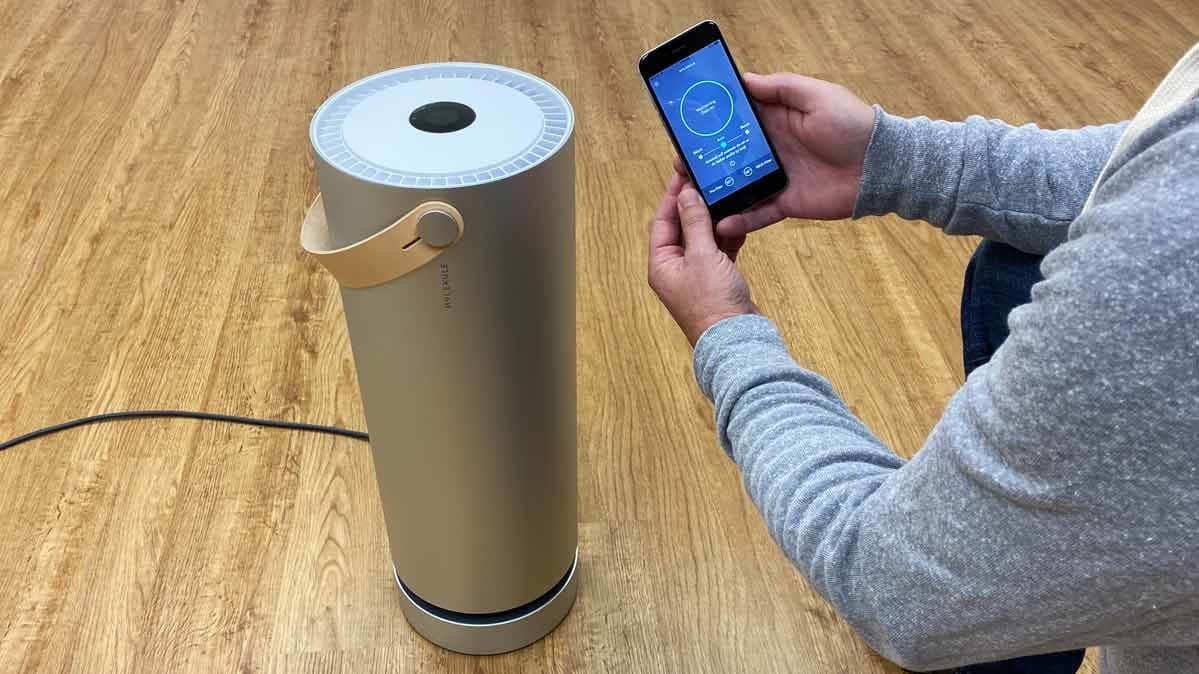 person holding smartphone with Molekule app in front of Molekule air purifier