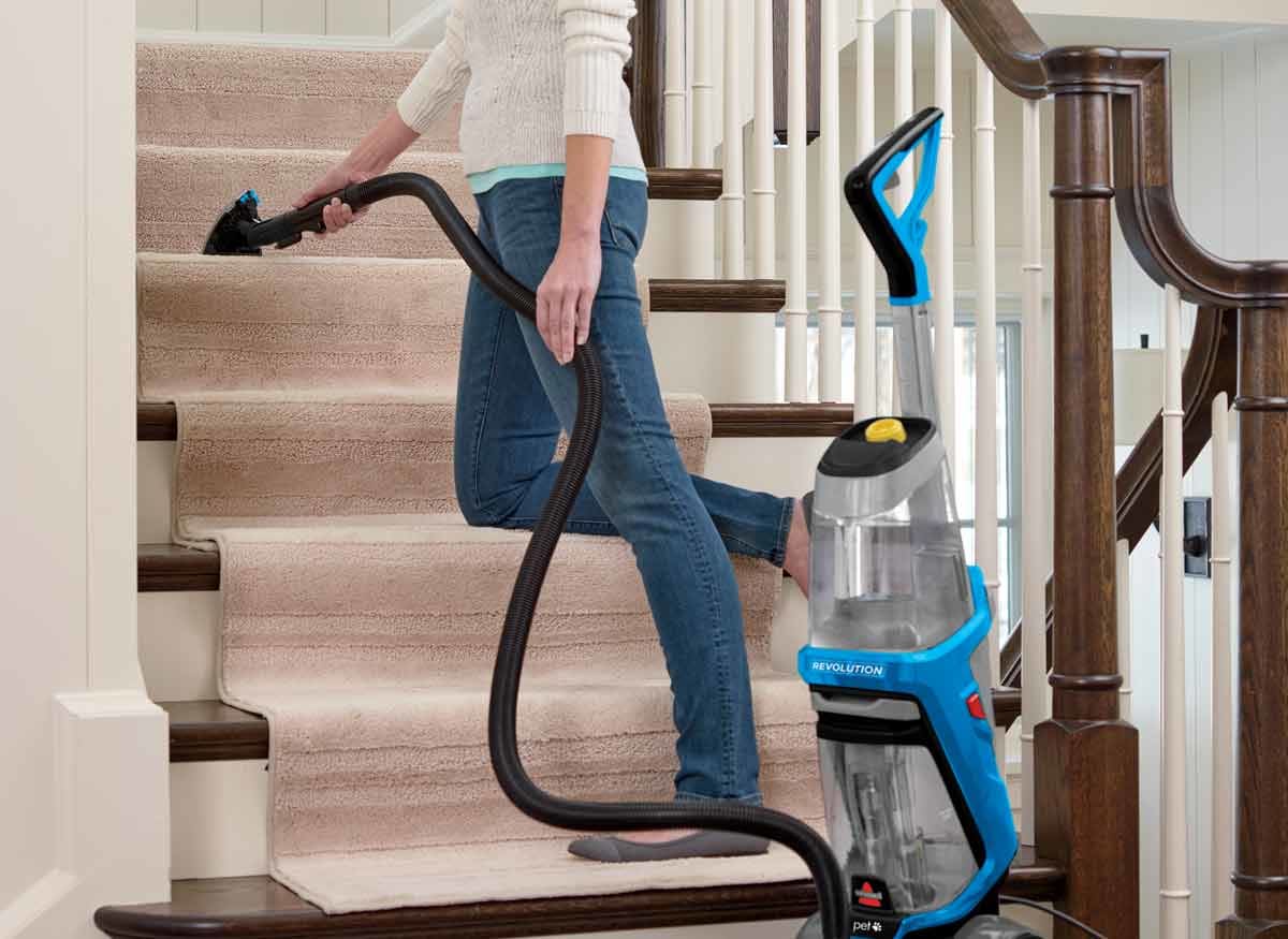 person cleaning carpet running on stairs using carpet cleaner with long hose