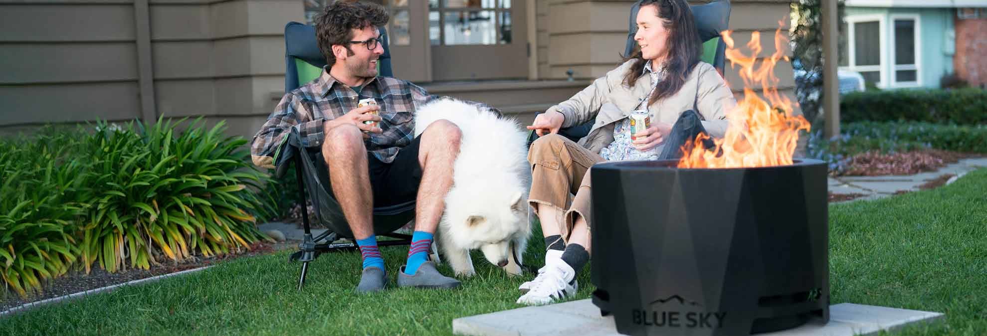 couple with dog sitting in lawn chairs around Blue Sky Outdoor Living Fire Pit