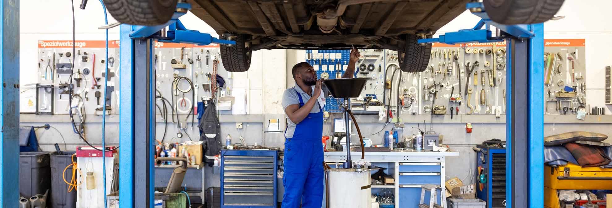 mechanic in auto repair shop changing oil under car that's raised up on lift