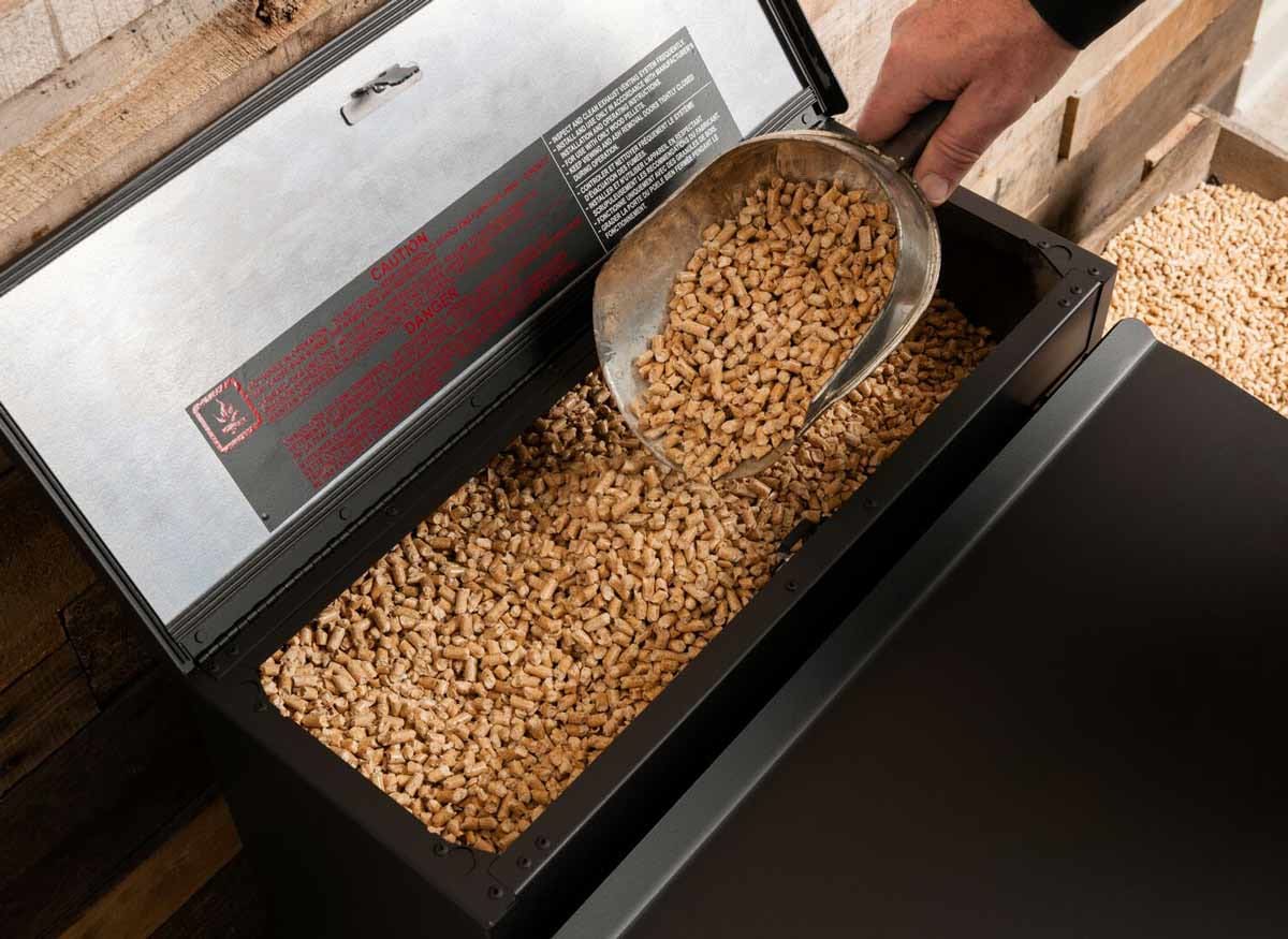 detail of person putting scoop of wood pellets into hopper of Harman Stove pellet stove
