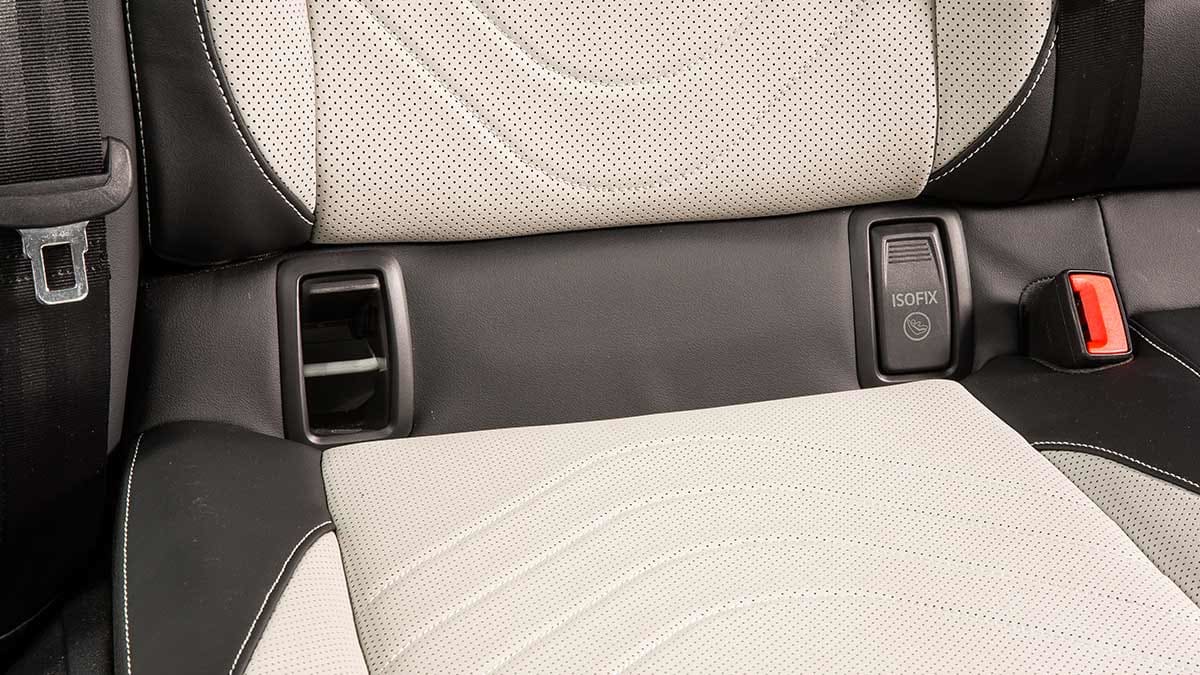 A close-up view of a car's rear seat crease showing two built-in lower anchor attachment points for installing a child safety seat. The right anchor is covered by a plastic flap labeled "ISOFIX" with a child seat icon, while the left anchor is open, exposing the metal bar.