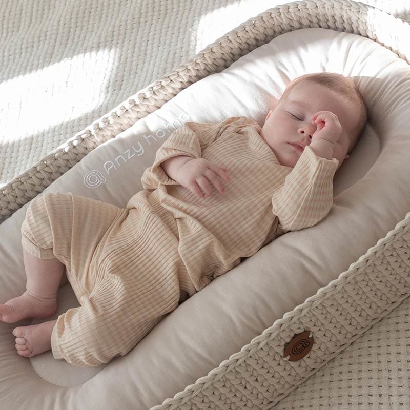 A baby asleep on their back in an Anzy Home Baby Lounging and Changing Basket.