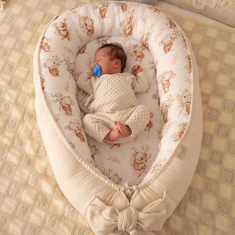 A baby seen from above asleep on their back in a CocoMi Premium Baby Nest with a pacifier in their mouth.