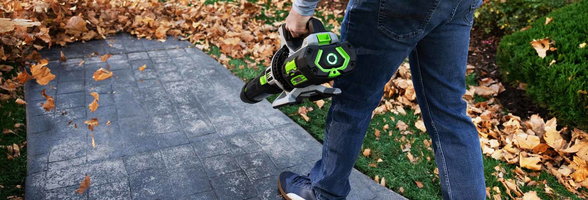 close up of person holding Ego LB8803 leaf blower to blow leaves off of grey brick walkway