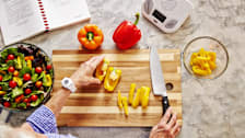 Woman in kitchen cutting peppers for salad wearing life alert device
