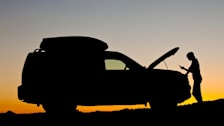 Car with hood open at sunset and person standing in front looking at phone