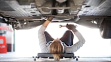 Female mechanic under a car doing repairs
