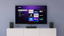 Wall mounted TV showing Roku interface, Roku speakers and Roku streambar on console table