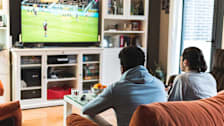 Two people watching soccer on a television