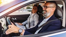 Two people driving in a car with the driver's window open
