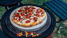 Pepperoni pizza with olives and mushrooms sitting on a kamado grill.
