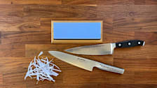 Sharp Pebble Stone knife sharpener seen on a cutting board with two sharp knives and strips of cut paper.