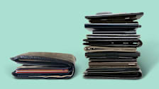 Old-fashioned bifold wallet stuffed with cards and money next to stack of  11 slim wallets.