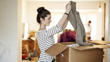 person in striped shirt folding sweater to put in cardboard box with more boxes and person in background
