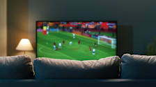 view of tv with soccer match from behind a grey couch
