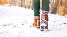 view of person's feet and legs walking on snow in wooded area while wearing hiking boots