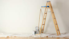 A room with a ladder and painting supplies.