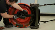 person replacing lawn mower blade with lawn mower tipped over on side