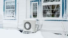 Heat pump covered in snow outside a house.