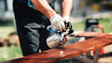 detail of person using paint sprayer to paint board brown