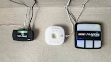 Tailwind IQ3 Smart Automatic Garage Controller Pro, Chamberlain my Q Smart Garage Control, and Genie Aladdin Connect Wi-Fi RetroFit Kit attached to wall in garage