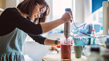 person in kitchen using immersion blender to blend fruit smoothie