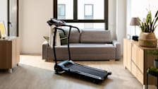 small living room with couch and dressers with treadmill in the center of the room