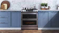 Samsung NE63T8751SG slide-in range in kitchen with blue cabinets and stainless steel pots and pans on the stovetop