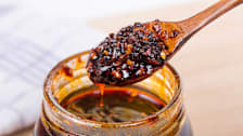 jar of Chinese style chili sauce with spoonful on wooden spoon over jar