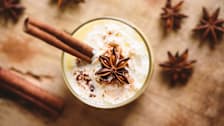 overhead view of drink with cinnamon stick and star anise pod with cinnamon sticks and star anise pods on wooden surface