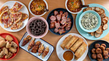 overhead view of spread of plated Superbowl snacks from Costco like spring rolls, chocolate pretzels, jalapeno poppers, chili, pizza, and spinach artichoke dip