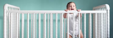 baby standing up and holding top of crib railing