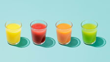 four glasses of different types of fruit juice on teal background