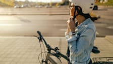 person on sidewalk clipping helmet while standing with their bike, cars and road in background