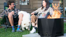 couple with dog sitting in lawn chairs around Blue Sky Outdoor Living Fire Pit