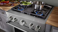 KitchenAid KFDC500JSS pro-style range with front burner on with a pot and pan on the burners