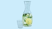 empty glass and pitcher of water with slices of lemon, cucumber, and basil leaves