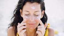 A woman putting sunscreen on their face.