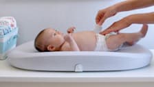 Baby on Hatch Grow Smart Changing Pad, mom adjusting diaper