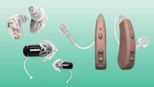 Three pairs of over-the-counter hearing aids on a green background